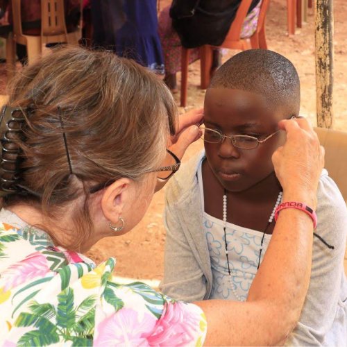 Pat fitting prescription glasses on a young lady in Lugazi